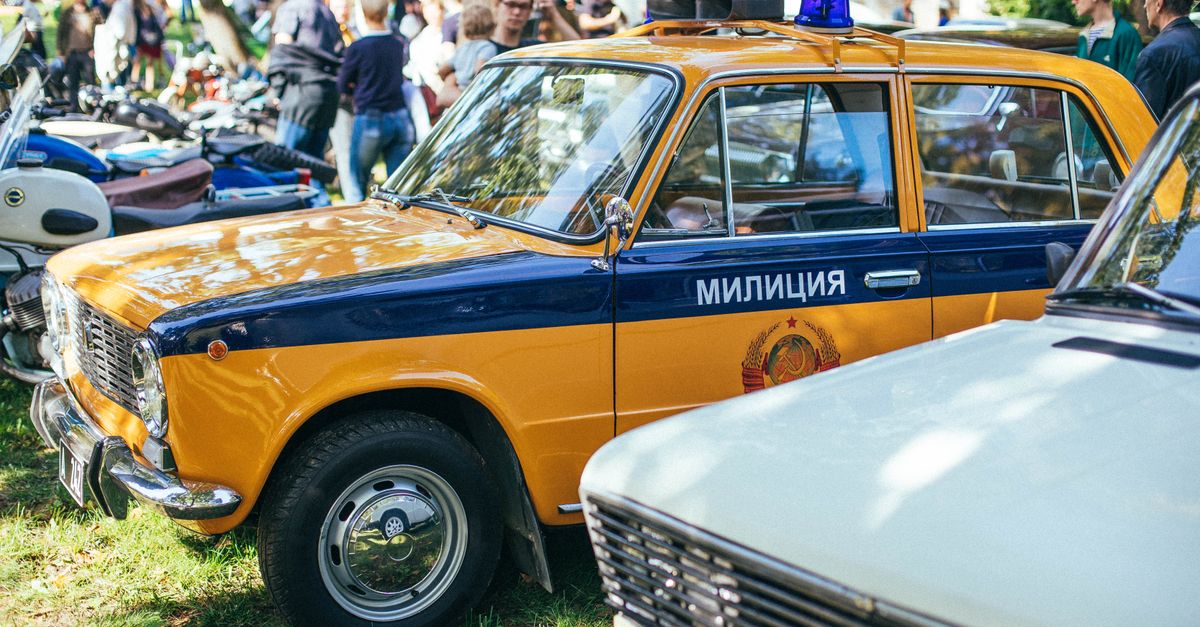 A vintage Soviet police car displayed at an outdoor event with a crowd in the background.